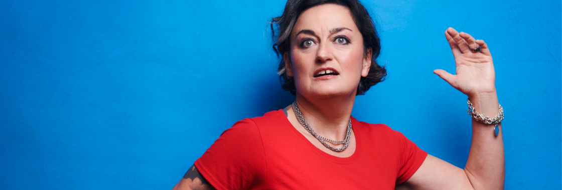 Portrait of comedian Zoe Lyons standing against a blue background